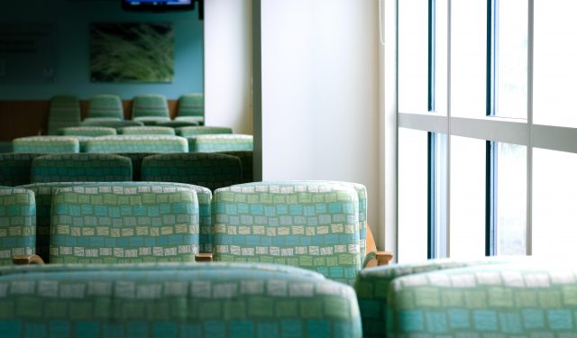 Empty green chairs of a waiting room next to a bright window